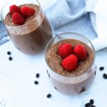 Two glass cups filled with chocolate chia pudding, topped with raspberries.