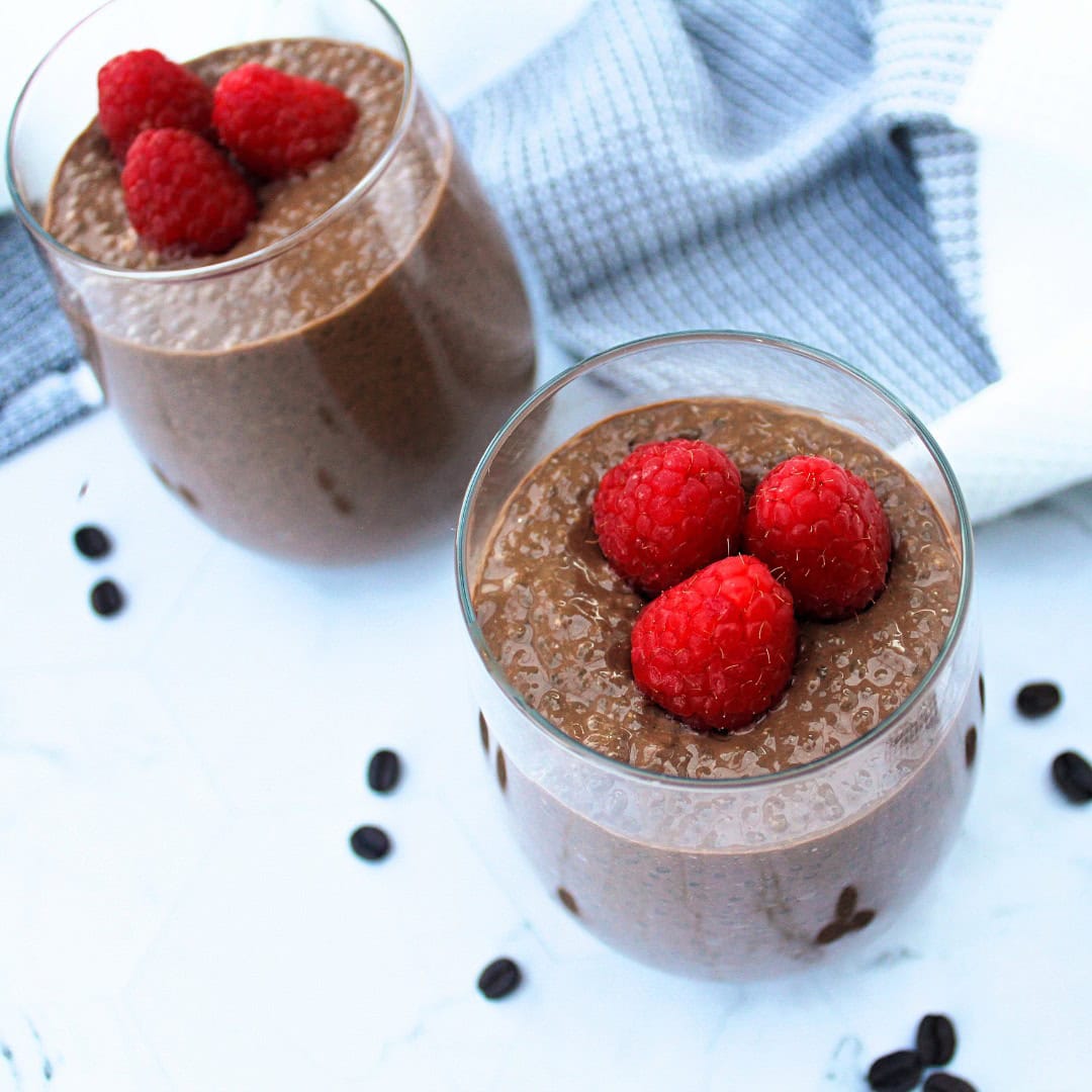 Two glass cups filled with chocolate chia pudding, topped with raspberries.