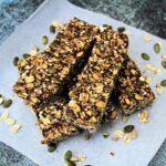 Stack of homemade granola bars, surrounded by oats and seeds.