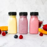 3 small bottles of drinkable yogurt surrounded by fresh fruit.